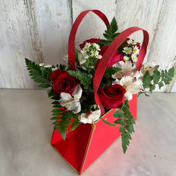 Red roses and white flowers in a red handled gift bag