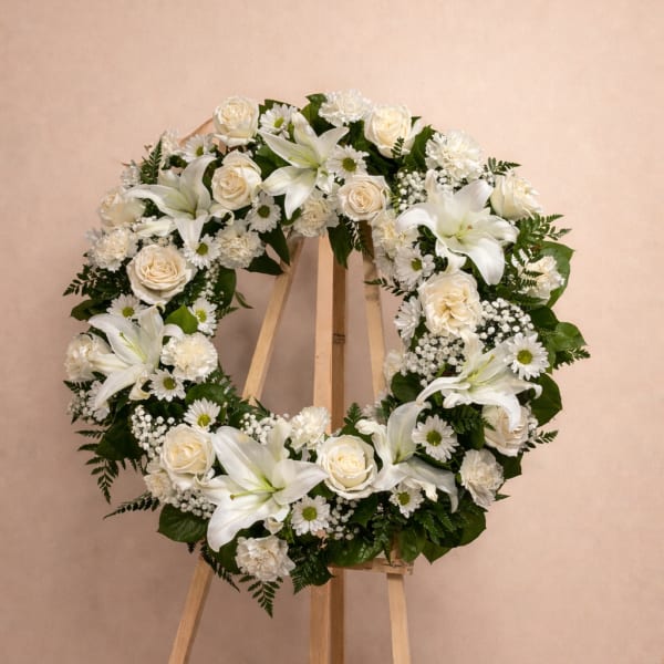 White floral wreath on a wooden easel with roses and lilies