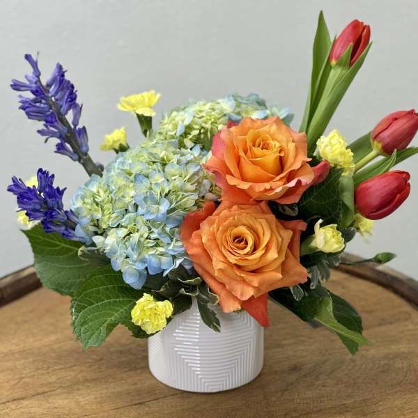 Orange roses with blue hydrangea and red tulips in a white vase