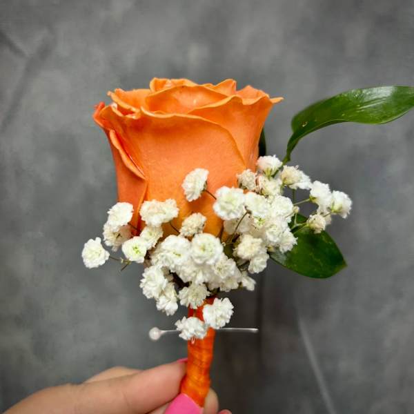 Orange rose boutonniere with white baby's breath and green leaves