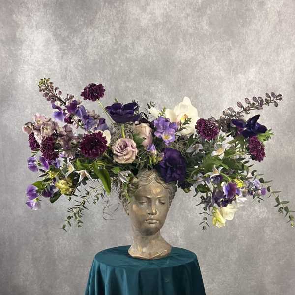 Purple and white floral arrangement in a sculpted head vase