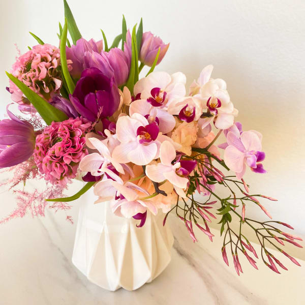 Pink and purple bouquet with orchids and tulips in a white vase