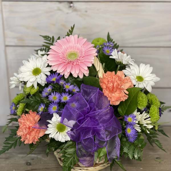 Mixed bouquet of daisies, gerbera, and carnations in a basket with a purple bow