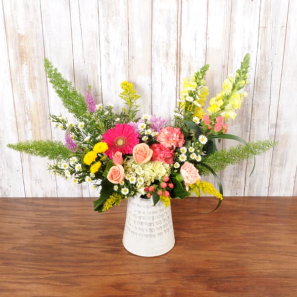 Asymmetrical mixed arrangement of pink, yellow and peach flowers in a white ceramic vase