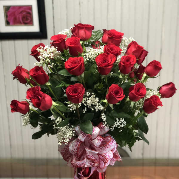 Red roses arranged in a tall red vase with a pink patterned ribbon
