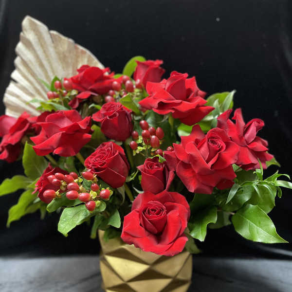 Red roses arranged in a gold geometric vase with berry accents