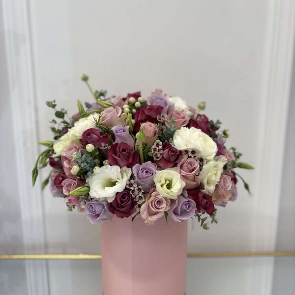 Mixed pink, lavender, and white roses arranged in a pink box
