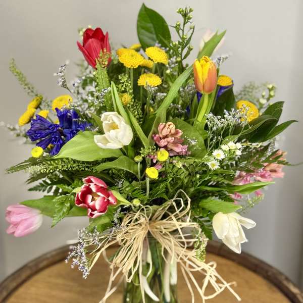 Mixed bouquet of colorful tulips and small flowers in a glass vase
