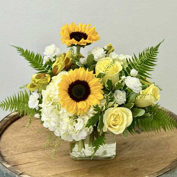 Yellow sunflowers and pale roses in a clear square vase