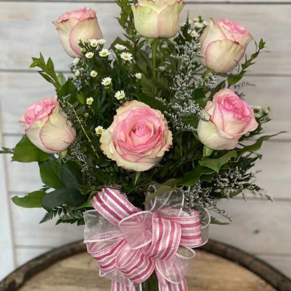 Pink and white roses arranged in a glass vase with a striped ribbon