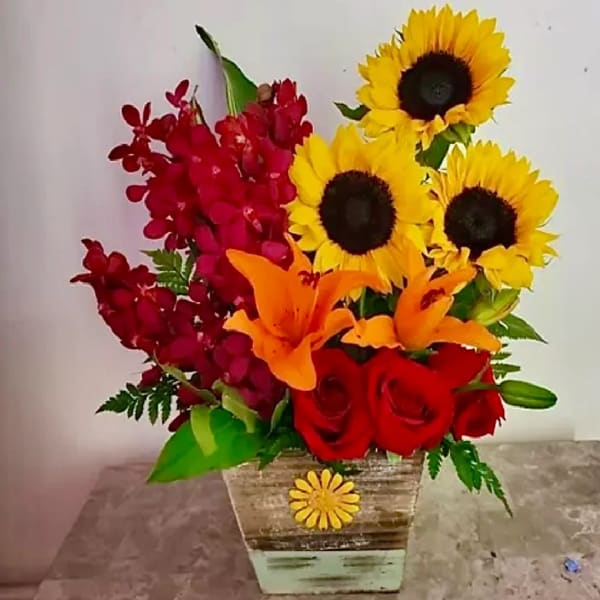 Bouquet of sunflowers, red roses, orange lilies, and red orchids in a wooden container