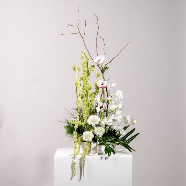 Tall floral arrangement with white and pale pink blooms in a white container
