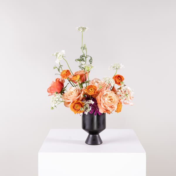 Peach and orange flower arrangement in a black vase