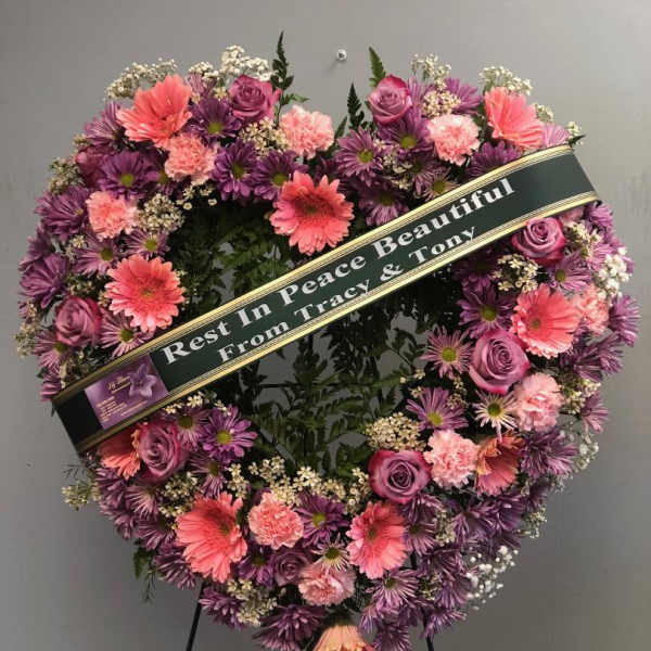 Heart-shaped funeral wreath with pink and purple flowers on a stand
