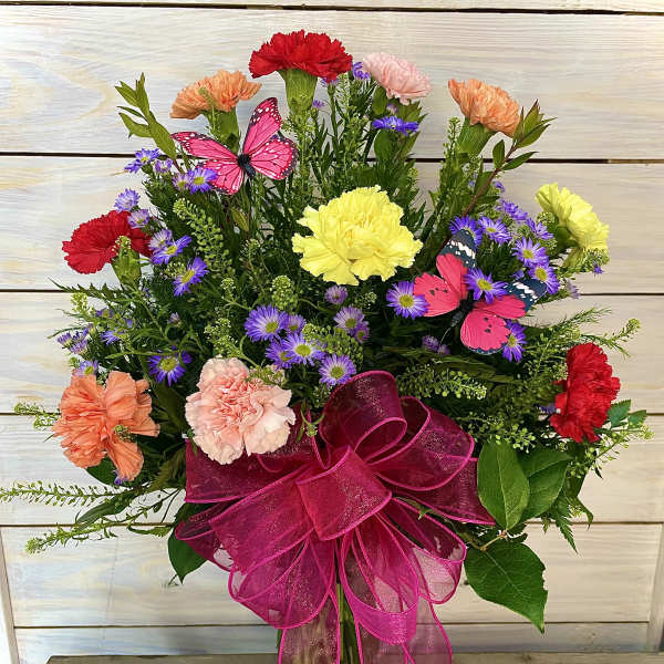 Colorful bouquet of carnations and purple daisies in a glass vase with a pink bow