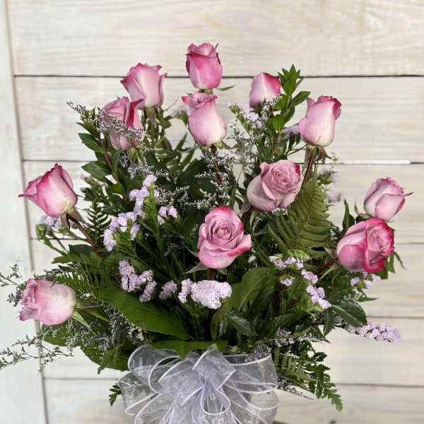 Pink roses arranged in a clear glass vase with a white ribbon bow