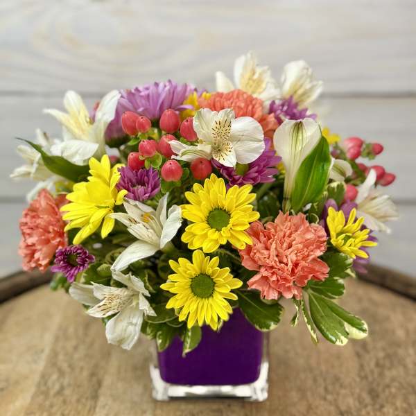 Colorful mixed bouquet in a purple vase with daisies, carnations, and white lilies