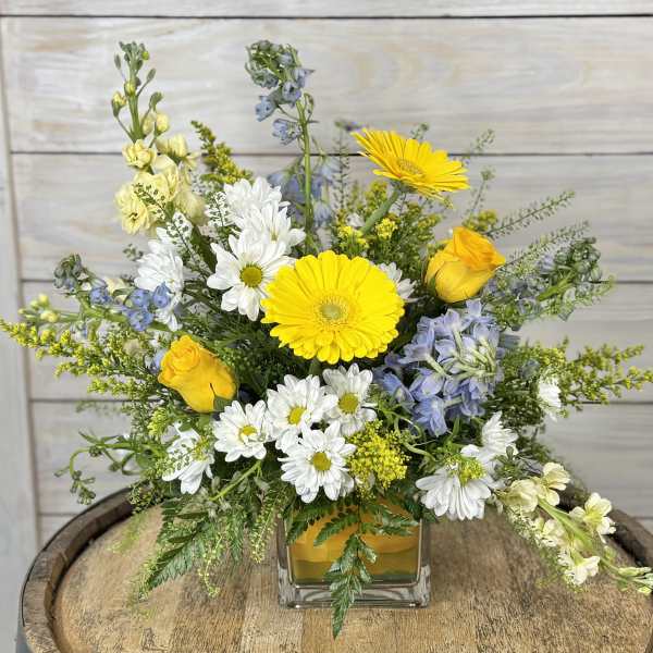 Mixed bouquet of yellow, white, and blue flowers in a glass vase