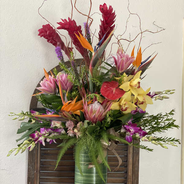 Tropical flower arrangement in a tall green vase with orchids and bird-of-paradise