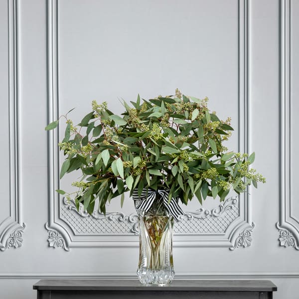Green foliage arrangement in a clear glass vase with a striped ribbon
