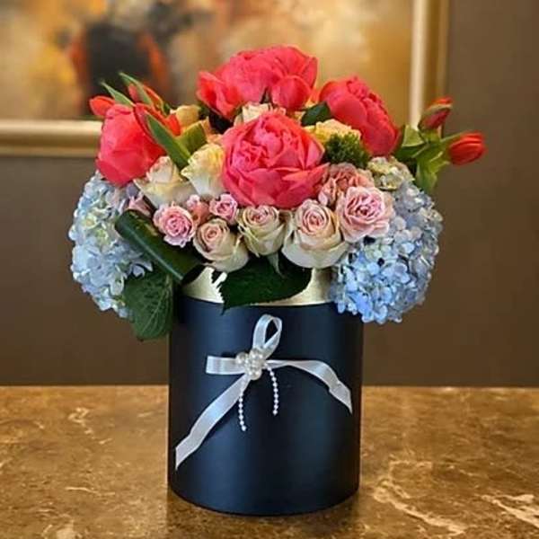 Pink and blue floral arrangement in a dark round box with a ribbon