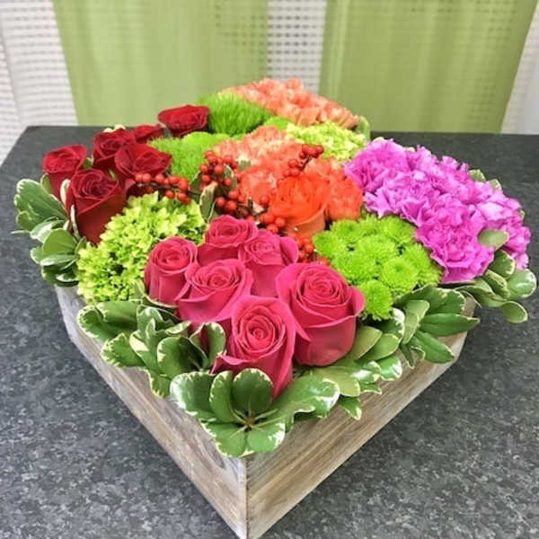 Square box arrangement of pink and red roses, green mums, orange carnations, and pink blooms in color-blocked sections