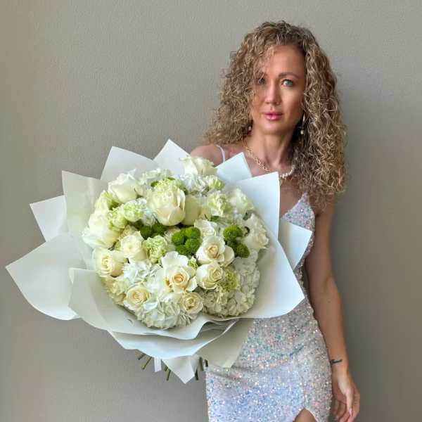 Woman holding a large bouquet of white roses and hydrangeas wrapped in white paper.