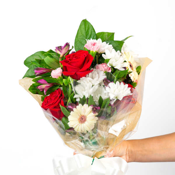 Handheld mixed bouquet with red roses, white mums, and pastel blooms wrapped in cellophane with a white bow