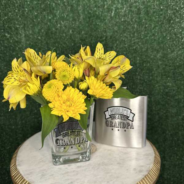 Yellow flowers in a glass vase beside a "World's Greatest Grandpa" mug