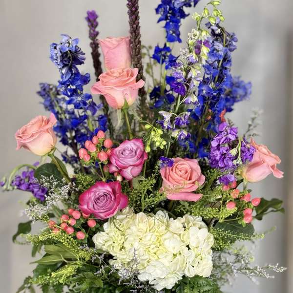 Tall bouquet of pink roses, blue flowers, and white hydrangeas in a glass vase