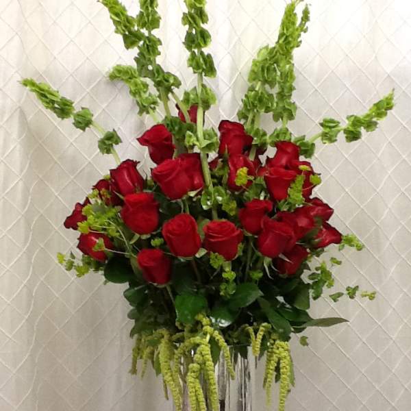 Red roses arranged in a tall silver vase with green filler flowers