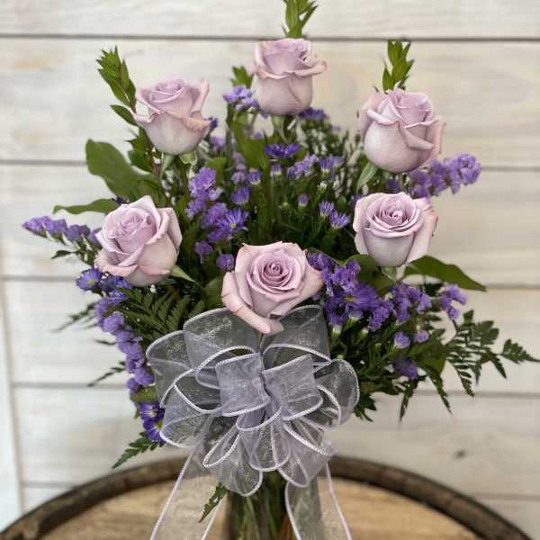 Lavender roses and purple filler flowers in a clear glass vase with a sheer bow