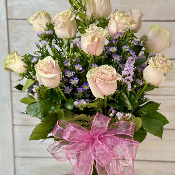 Bouquet of pale pink roses and purple filler flowers in a glass vase with a pink ribbon