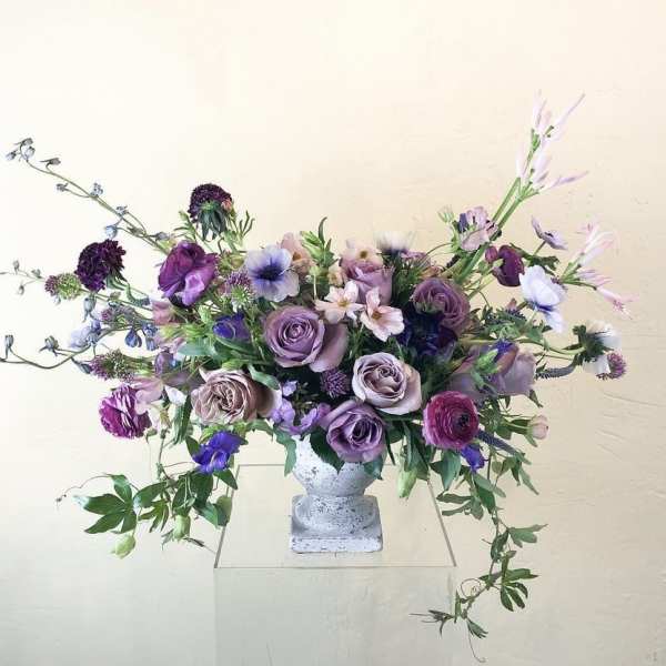 Lavender and purple floral arrangement in a white pedestal vase