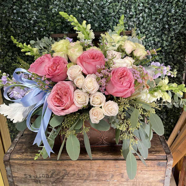 Pink and cream roses arranged in a wooden box with a blue ribbon