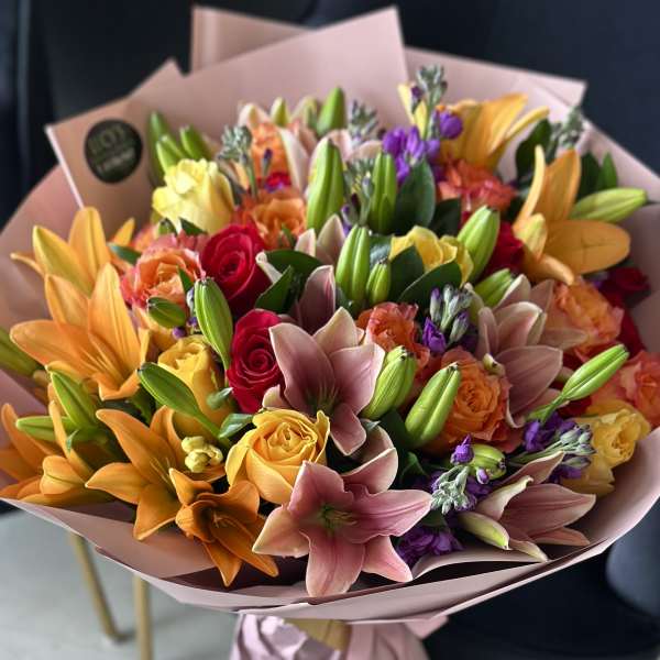 Mixed bouquet of lilies, roses, and purple flowers wrapped in pink paper