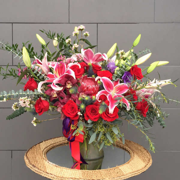 Large mixed bouquet of red roses, pink lilies, and orchids in a glass vase