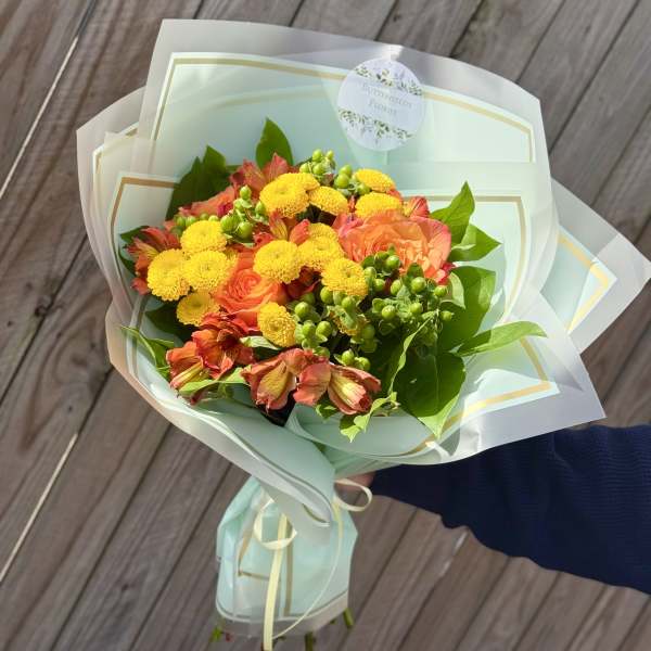 Bouquet of orange and yellow flowers wrapped in pale blue paper