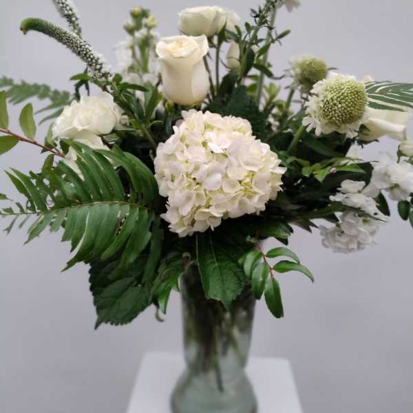 White floral arrangement in a glass vase with roses and hydrangea