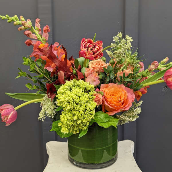 Mixed bouquet in a green glass vase with orange and pink flowers