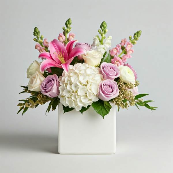 Pink lilies and roses arranged in a white square vase