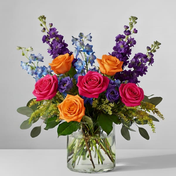 Bouquet of pink and orange roses with purple and blue flowers in a glass vase