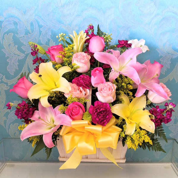 Pink and yellow lilies with roses in a wooden basket tied with a yellow bow