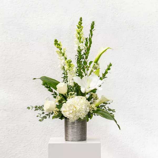 White floral arrangement in a silver vase with tall green accents