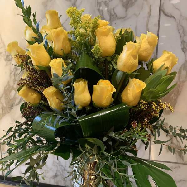 Yellow roses arranged in a gold vase with mixed greenery