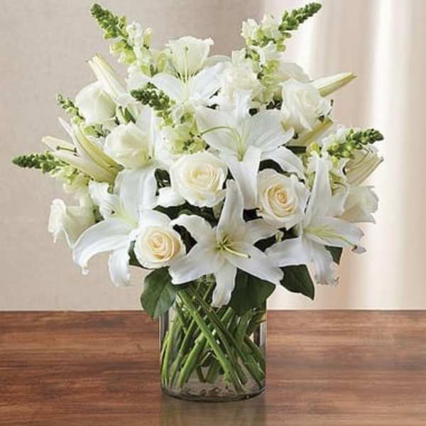 Arrangement of white lilies, roses, and snapdragons in a clear glass cylinder vase