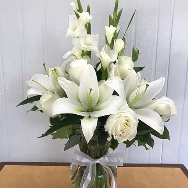 White lilies and roses arranged in a glass vase with a ribbon