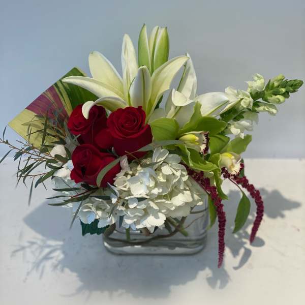 Red roses and white lilies in a clear glass vase with white hydrangea
