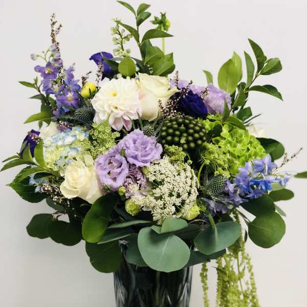 Mixed bouquet of purple, white, and green flowers in a tall dark vase
