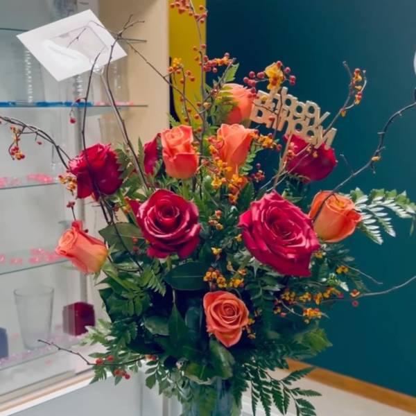 Mixed rose arrangement in a glass vase with a birthday sign